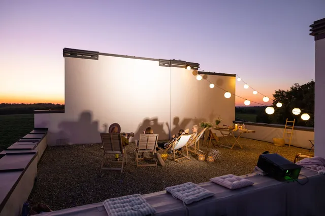 Rooftop patio at dusk with seating, string lights, and figures enjoying the evening.
